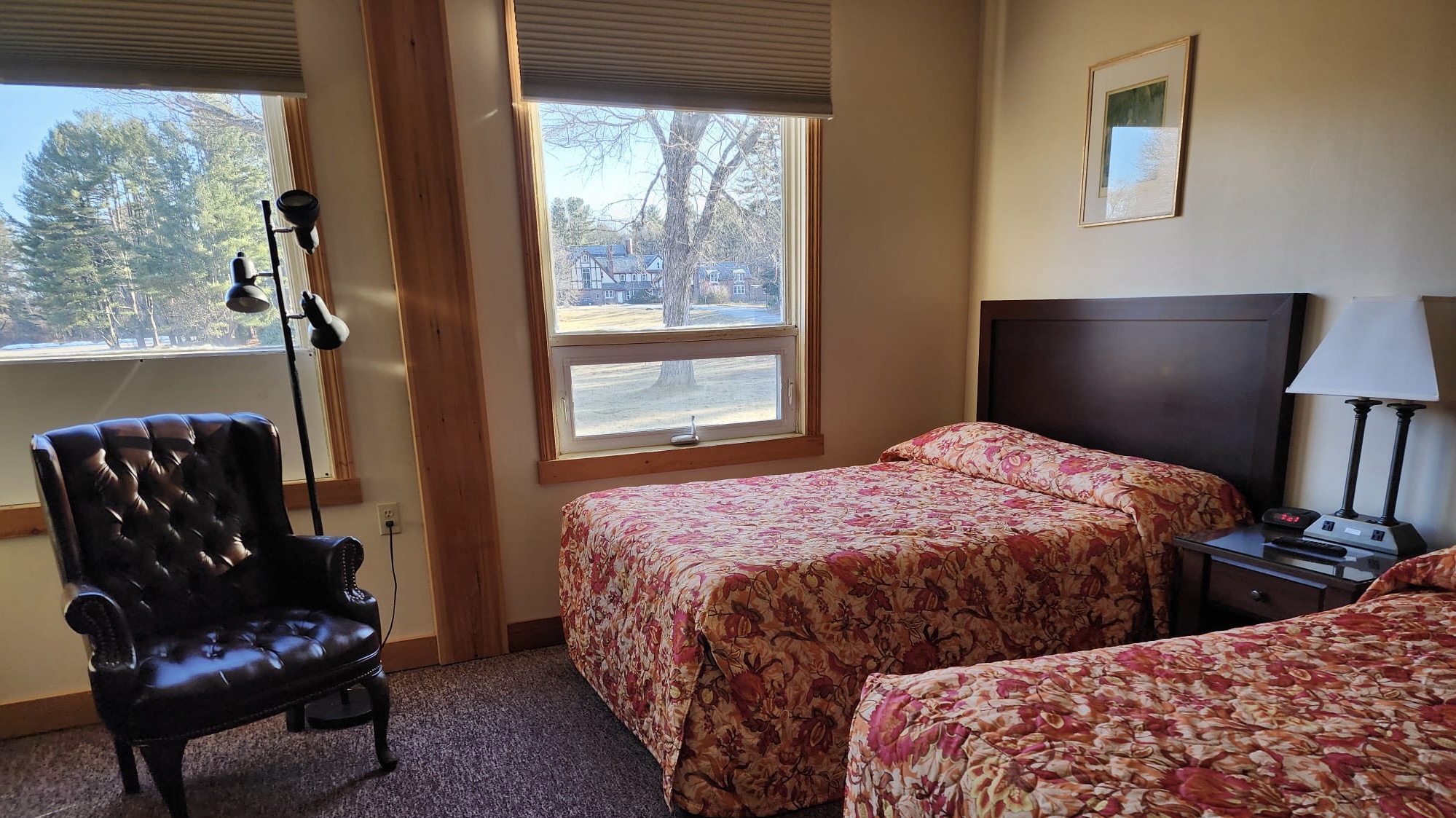 A guest room featuring two beds, a sofa, bedside table, and windows overlooking a lawn.