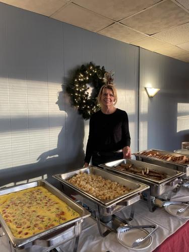 A chef standing over four chafing dishes with eggs, potatoes, sausages, and waffles in a dining room. 