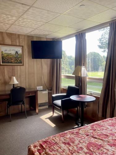 Guest room featuring a desk, sofa, small table, lamp, TV, and windows overlooking a green lawn. 