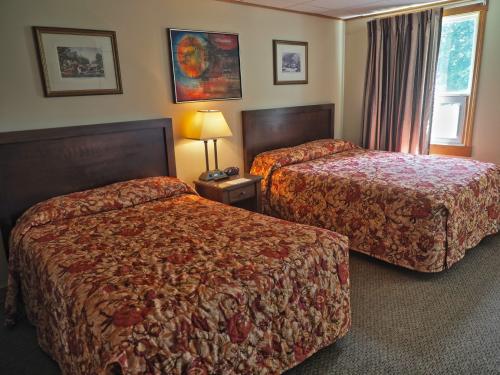 A cozy guest room with two beds, nightside table, lamp, and paintings on the wall.