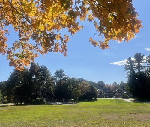 Green lawn with monastery and forest in the background, framed by fall tree branches and leaves.